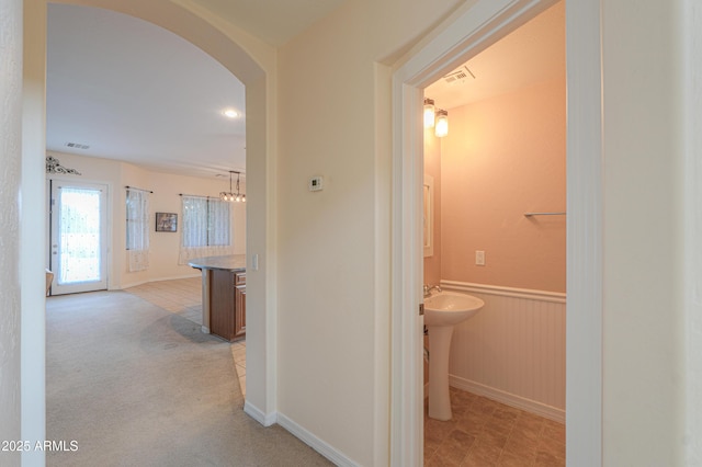 hallway featuring a wainscoted wall, visible vents, arched walkways, and light colored carpet