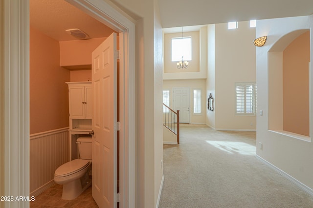 bathroom featuring a chandelier, toilet, a wainscoted wall, visible vents, and a towering ceiling