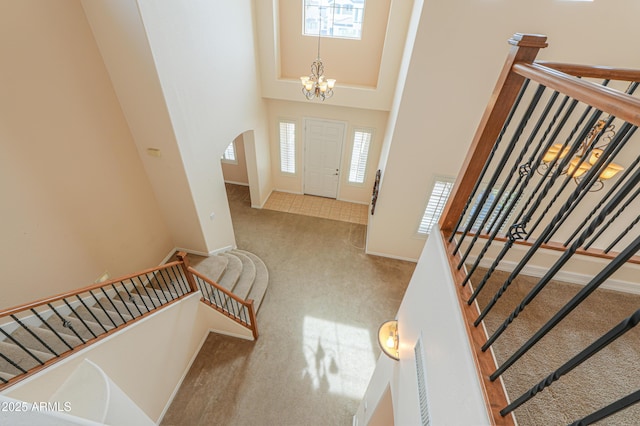 carpeted entrance foyer featuring arched walkways, a high ceiling, a chandelier, baseboards, and stairs