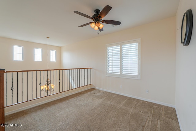 carpeted spare room featuring baseboards, a wealth of natural light, and ceiling fan with notable chandelier