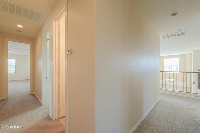 hall with light carpet, baseboards, and visible vents