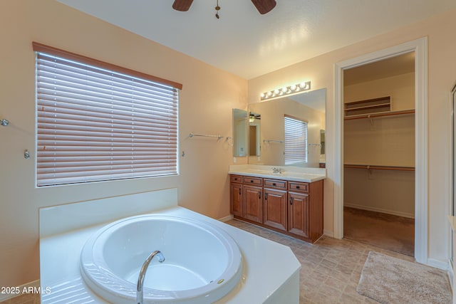 bathroom featuring ceiling fan, a garden tub, vanity, baseboards, and a walk in closet