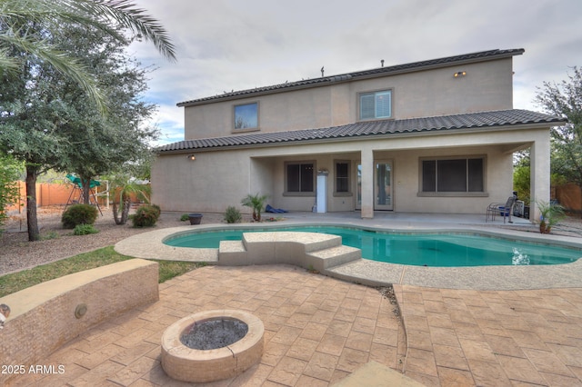 back of property featuring a patio area, a fire pit, a fenced in pool, and stucco siding