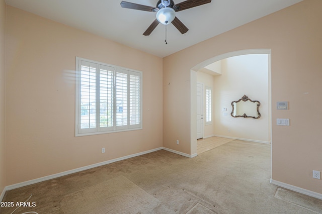 carpeted empty room with baseboards, arched walkways, and ceiling fan