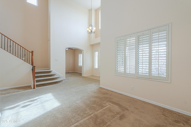 carpeted entrance foyer with arched walkways, a notable chandelier, stairway, a high ceiling, and baseboards