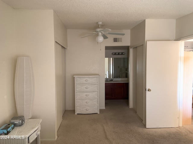 unfurnished bedroom featuring ensuite bathroom, light colored carpet, a textured ceiling, and ceiling fan