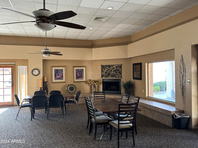 carpeted dining room featuring a fireplace, ceiling fan, and a drop ceiling