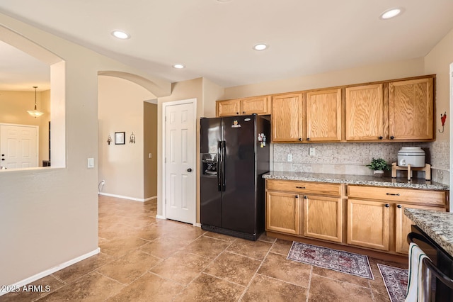 kitchen featuring decorative backsplash, light stone countertops, arched walkways, and black refrigerator with ice dispenser