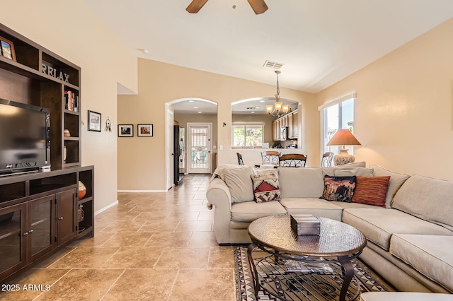 living room featuring stone tile flooring, baseboards, visible vents, ceiling fan with notable chandelier, and arched walkways