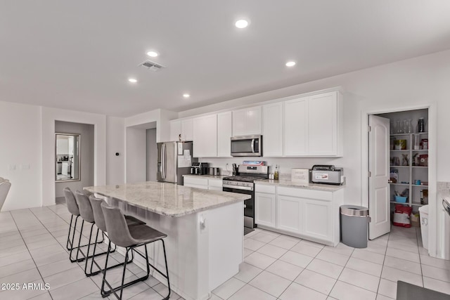 2347 W Sunland Ave, Phoenix, AZ 85041 - kitchen with stainless steel appliances, a breakfast bar area, a center island, white cabinetry, and light stone counters