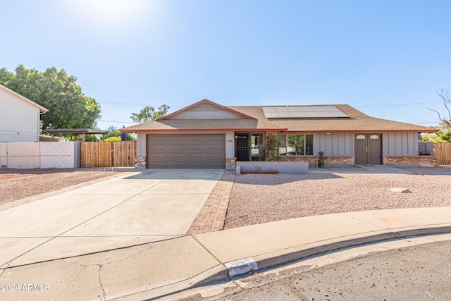 single story home with a garage and solar panels