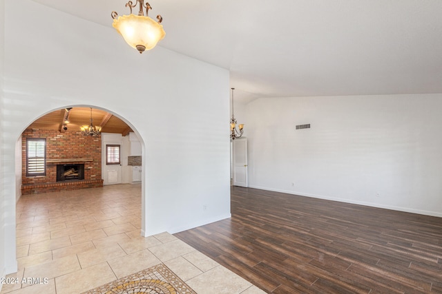 unfurnished living room featuring light wood-type flooring, lofted ceiling, an inviting chandelier, and a brick fireplace