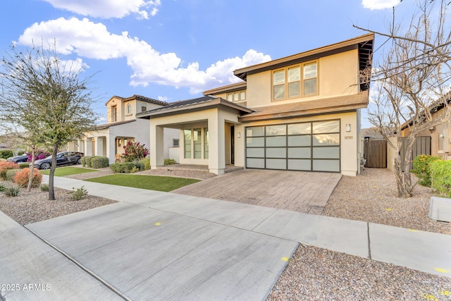 view of front of house with decorative driveway, an attached garage, fence, and stucco siding