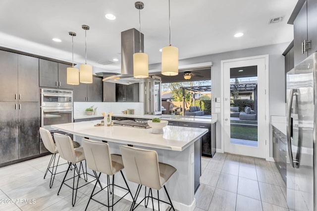 kitchen featuring a breakfast bar, island exhaust hood, stainless steel appliances, tasteful backsplash, and light countertops