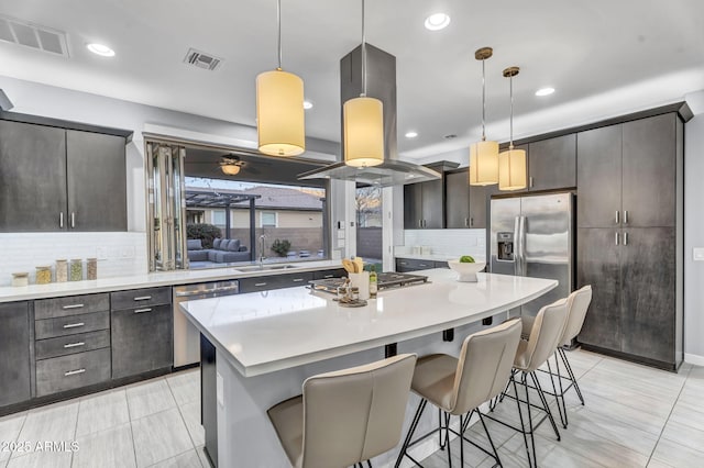 kitchen featuring island range hood, visible vents, appliances with stainless steel finishes, a breakfast bar, and a sink