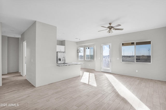 unfurnished living room with ceiling fan, sink, and light hardwood / wood-style floors