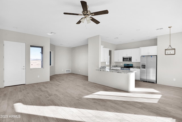 kitchen with kitchen peninsula, appliances with stainless steel finishes, light stone countertops, sink, and white cabinets