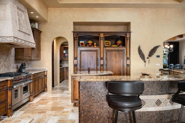 11457 E Salero Dr, Scottsdale, AZ 85262 - kitchen with custom range hood, a breakfast bar, range with two ovens, arched walkways, and stone tile floors