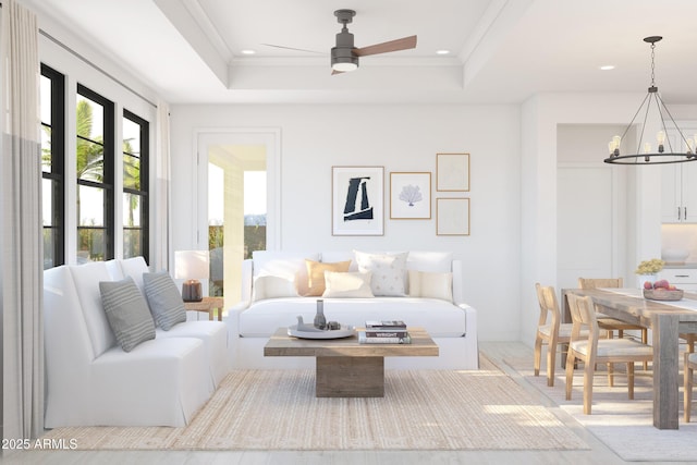 living room with crown molding, a tray ceiling, and ceiling fan with notable chandelier