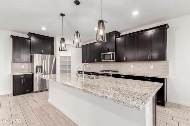 kitchen featuring appliances with stainless steel finishes, decorative light fixtures, a kitchen island with sink, and sink