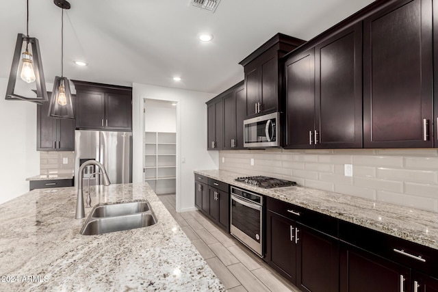 kitchen with appliances with stainless steel finishes, light stone countertops, sink, dark brown cabinets, and decorative light fixtures