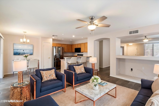 living room with ceiling fan with notable chandelier and dark hardwood / wood-style flooring