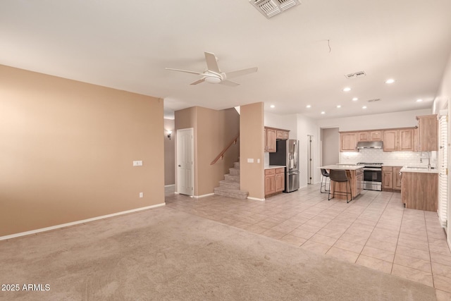 kitchen with a breakfast bar, appliances with stainless steel finishes, backsplash, a center island, and light colored carpet