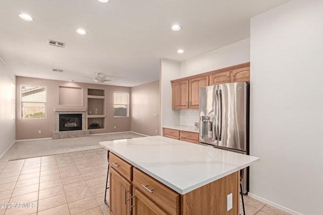 kitchen featuring a tile fireplace, a kitchen breakfast bar, a center island, ceiling fan, and stainless steel fridge with ice dispenser