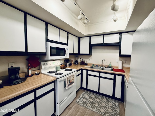 kitchen with white appliances, a sink, light countertops, ornamental molding, and a raised ceiling