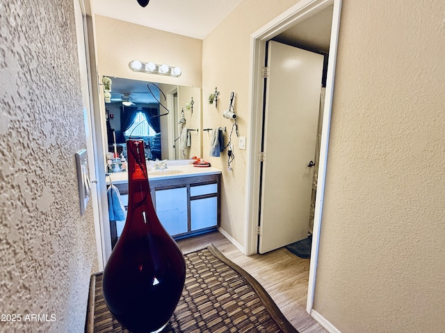 interior space featuring ceiling fan, a textured wall, wood finished floors, vanity, and baseboards