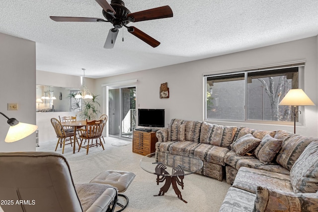 living room featuring ceiling fan with notable chandelier, light colored carpet, and a textured ceiling