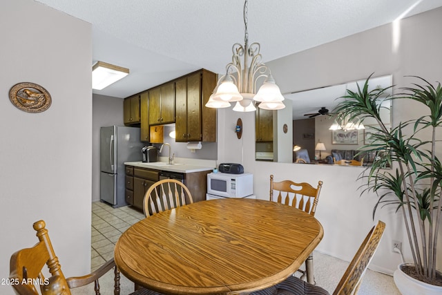 dining space with sink, ceiling fan with notable chandelier, and a textured ceiling