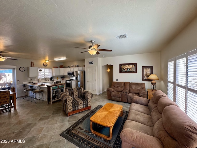 living area with ceiling fan, a textured ceiling, plenty of natural light, and visible vents