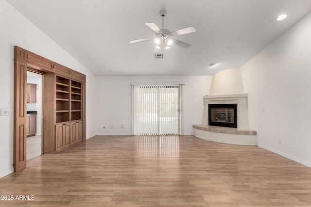 unfurnished living room with ceiling fan, a large fireplace, built in features, and light hardwood / wood-style flooring