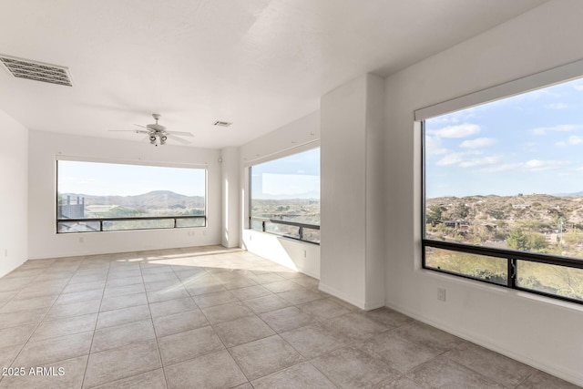 empty room featuring a wealth of natural light, a mountain view, ceiling fan, and light tile patterned flooring