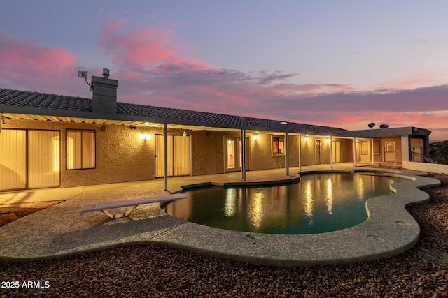 pool at dusk featuring a diving board and a patio area