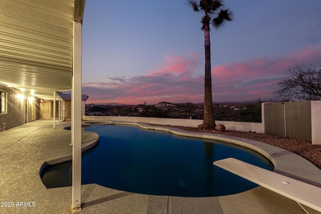 pool at dusk with a diving board and a patio area