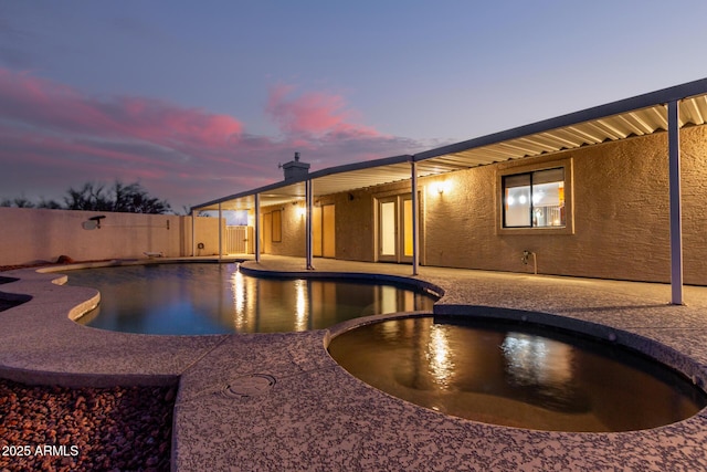 pool at dusk featuring a patio area and an in ground hot tub