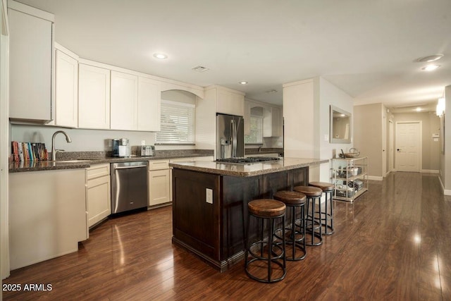 kitchen with appliances with stainless steel finishes, a center island, dark wood-type flooring, white cabinetry, and dark stone counters