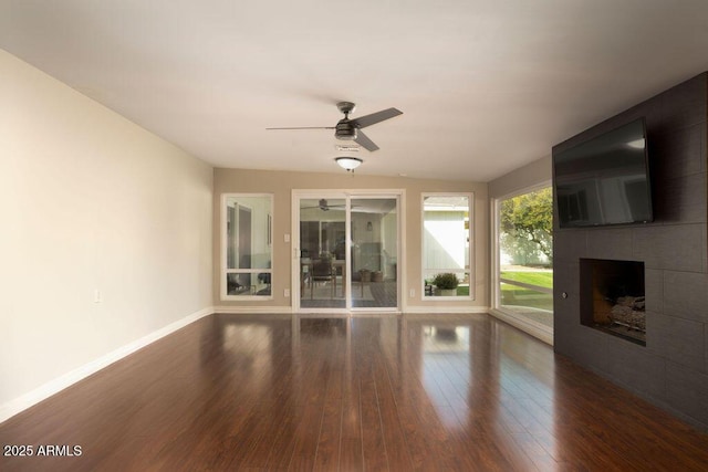 unfurnished living room with ceiling fan, dark wood-type flooring, and a tile fireplace