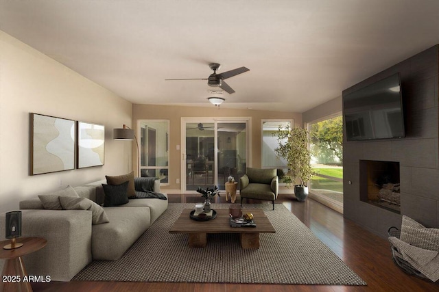 living room featuring ceiling fan, a tiled fireplace, and dark hardwood / wood-style floors