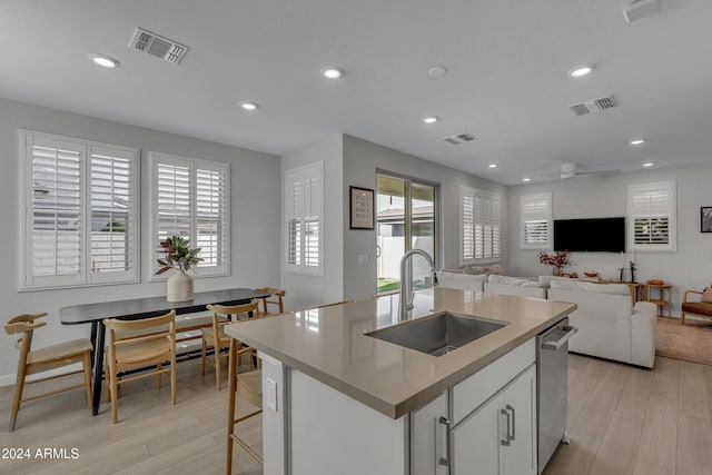 kitchen with a center island with sink, sink, plenty of natural light, white cabinets, and light wood-type flooring