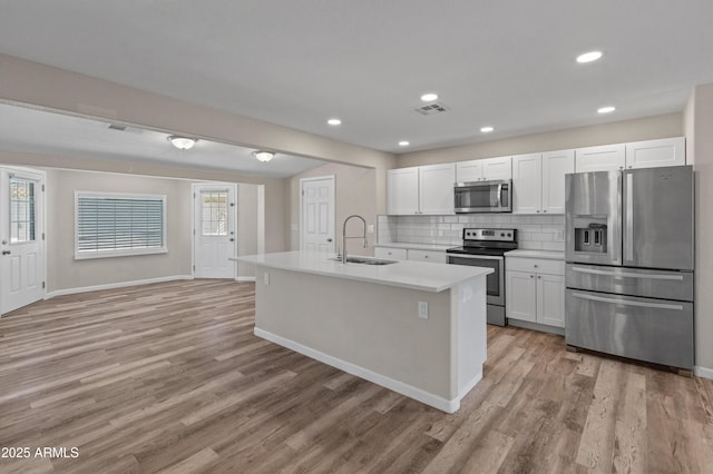 kitchen featuring light countertops, stainless steel appliances, a sink, light wood-style floors, and backsplash