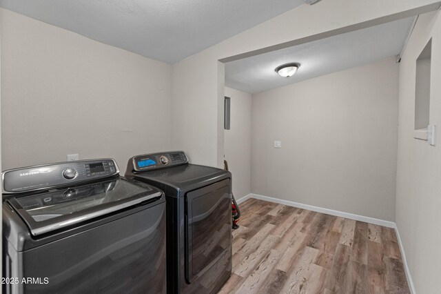 clothes washing area with washer and clothes dryer, light wood-style flooring, and baseboards