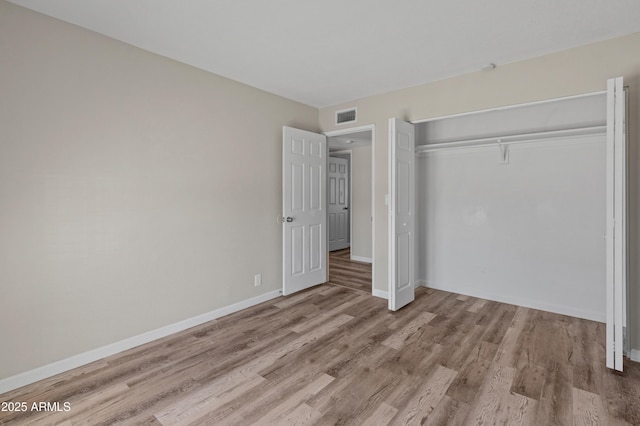unfurnished bedroom featuring wood finished floors, a closet, baseboards, and visible vents