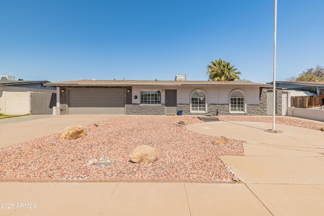 ranch-style house featuring fence, an attached garage, stone siding, and concrete driveway