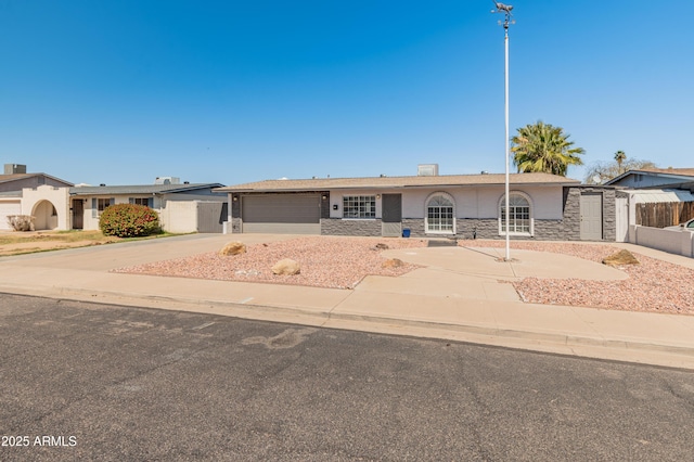 single story home with fence, an attached garage, stone siding, and concrete driveway