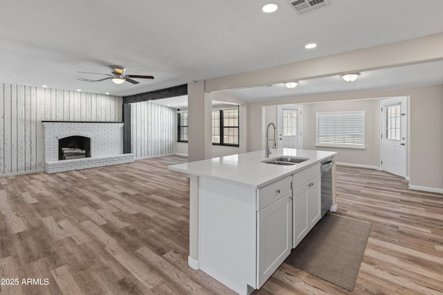 kitchen featuring light countertops, a center island with sink, a sink, visible vents, and light wood-style flooring