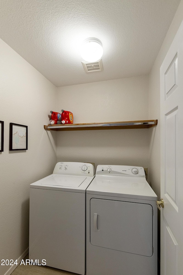 clothes washing area with washing machine and dryer and a textured ceiling