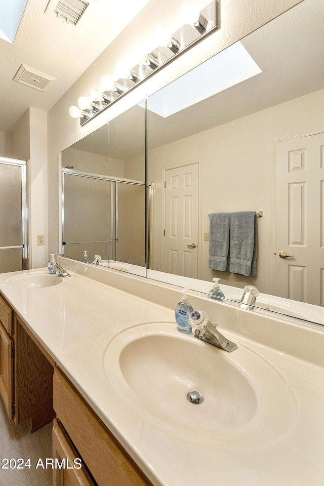 bathroom with vanity, a skylight, and a shower with door